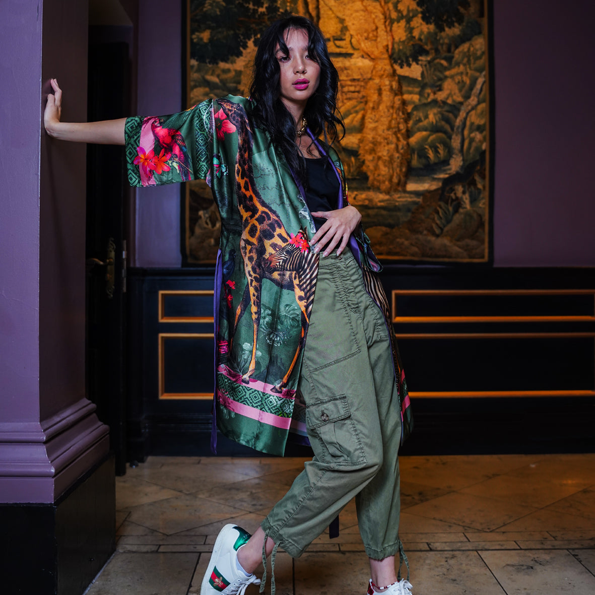 A female model wearing luxury 100% silk Kimono in a maximalist Carnival inspired design against an olive background