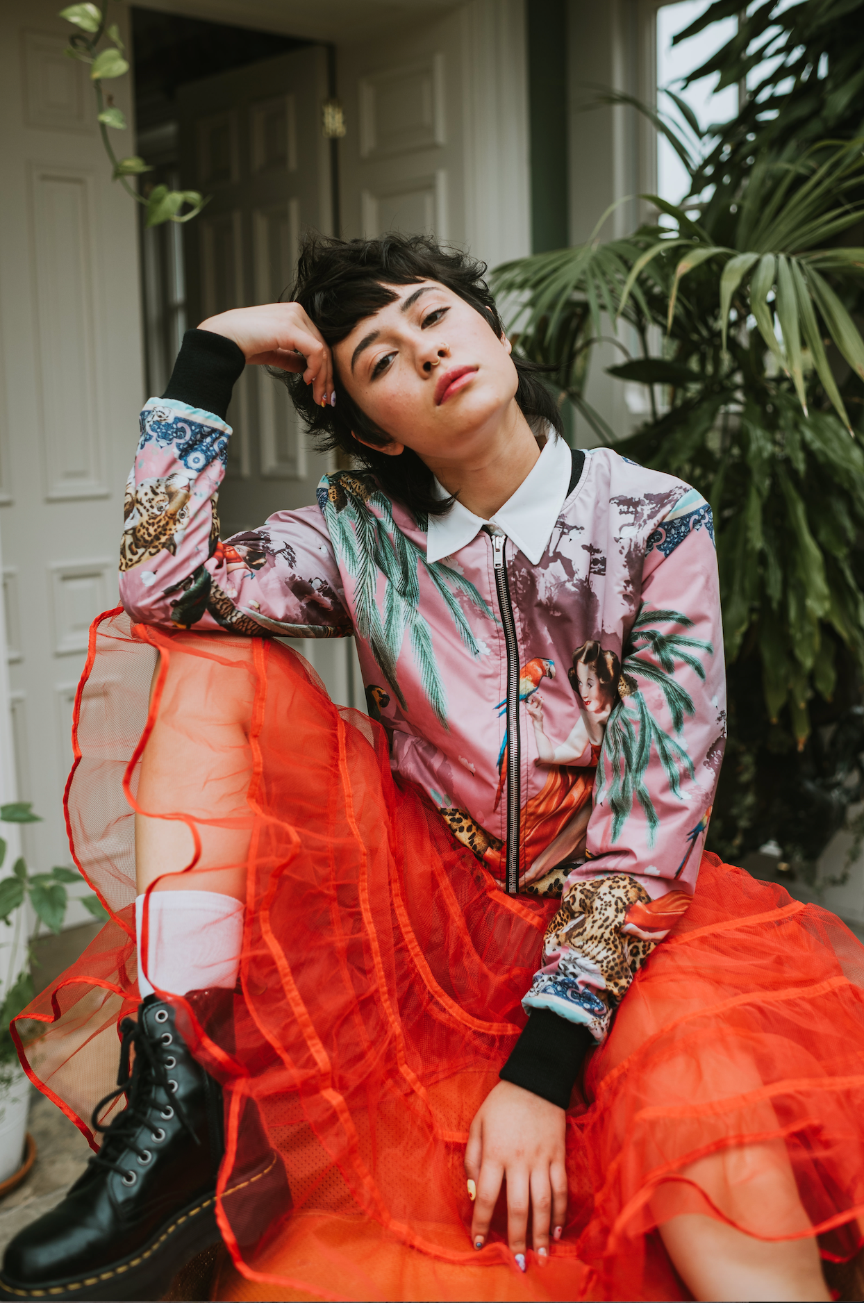 A  female model seated wearing luxury softshell bomber jacket in a maximalist vintage pink design