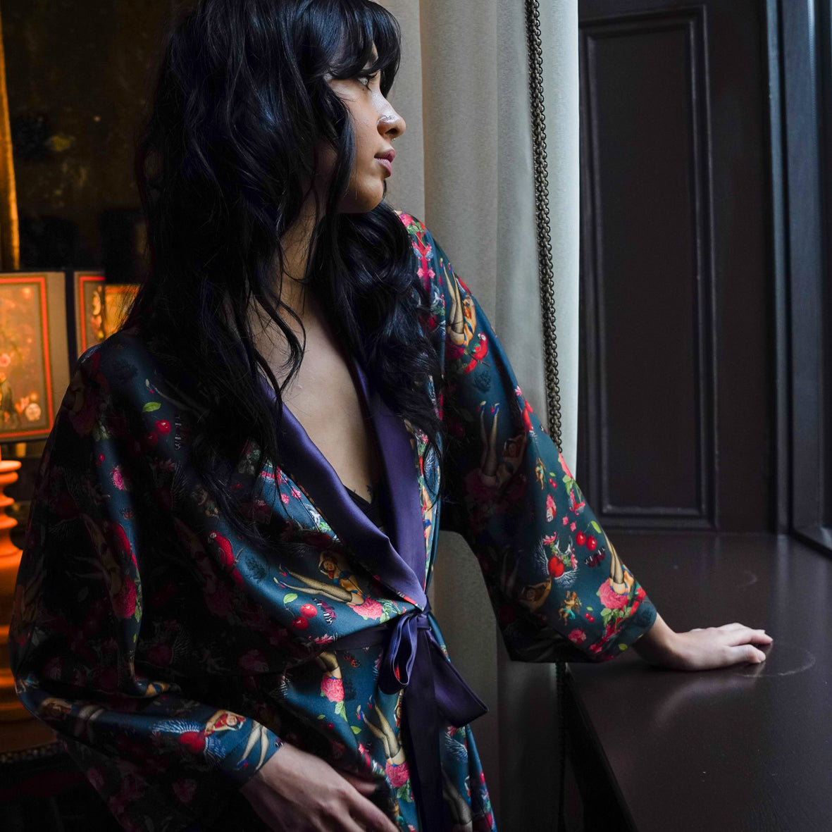 Model wearing luxury 100% silk kimono in a maximalist retro pinup design with cherries looking out window