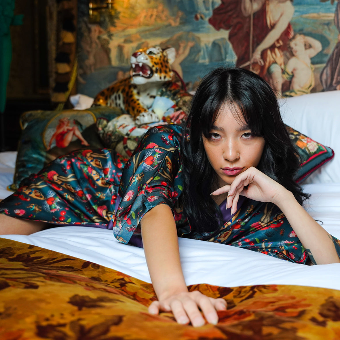 Female model lying on a bed wearing luxury 100% silk kimono in a maximalist retro pinup design with cherries