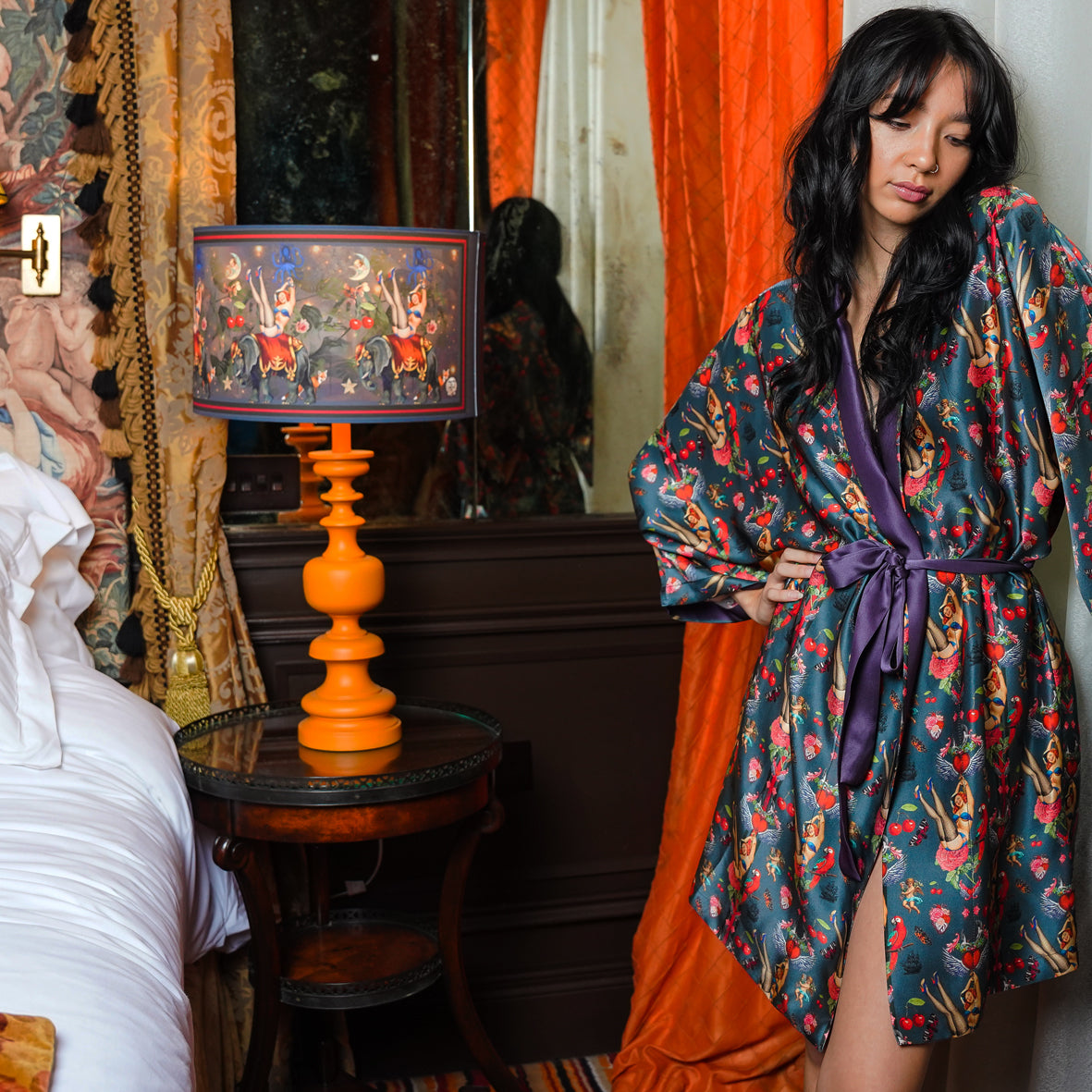 Female model wearing luxury 100% silk kimono in a maximalist retro pinup design with cherries with lampshade beside her