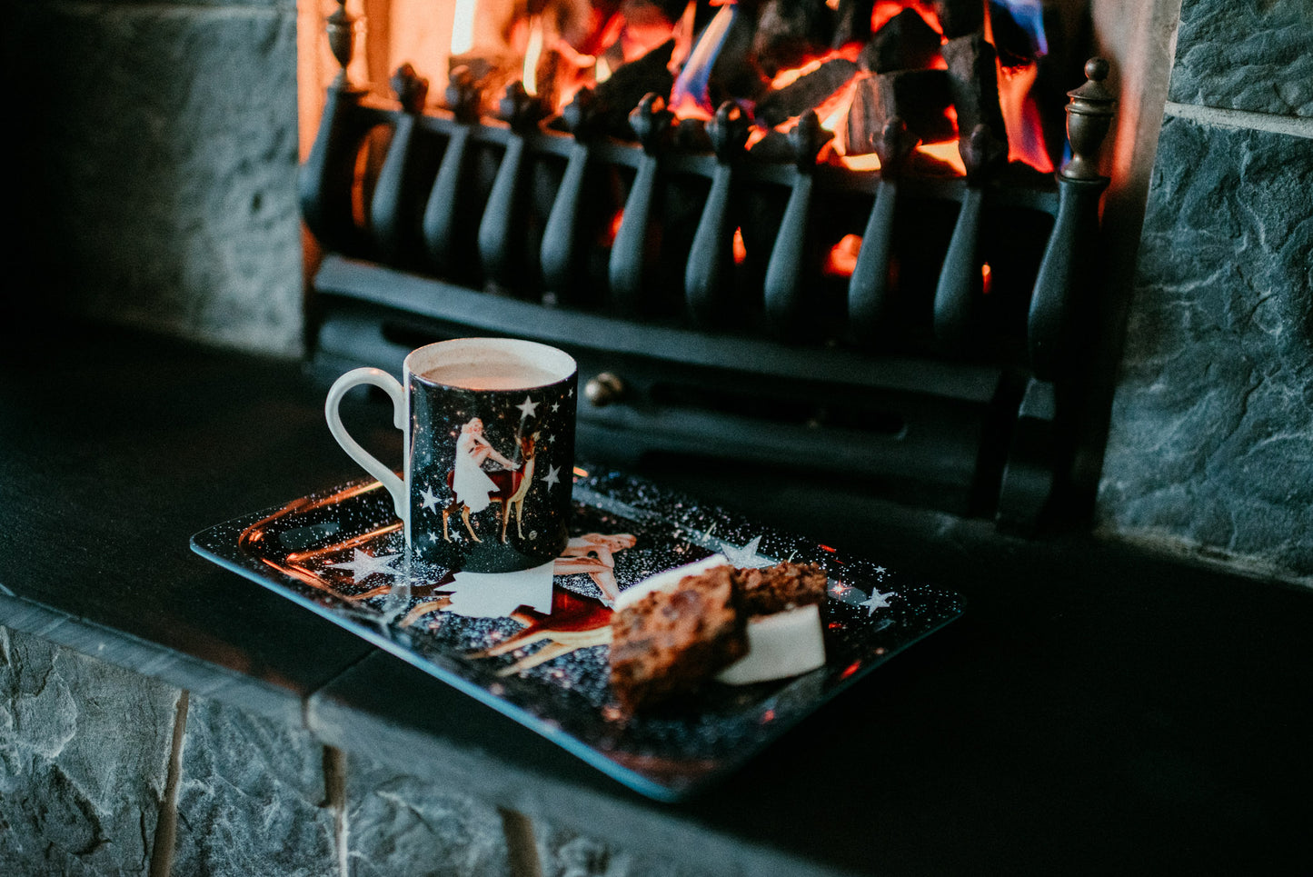 Luxury bone china coffee cup in a maximalist festive astrology design called - festive celeste placed on a tray with cake in front of a fireplace