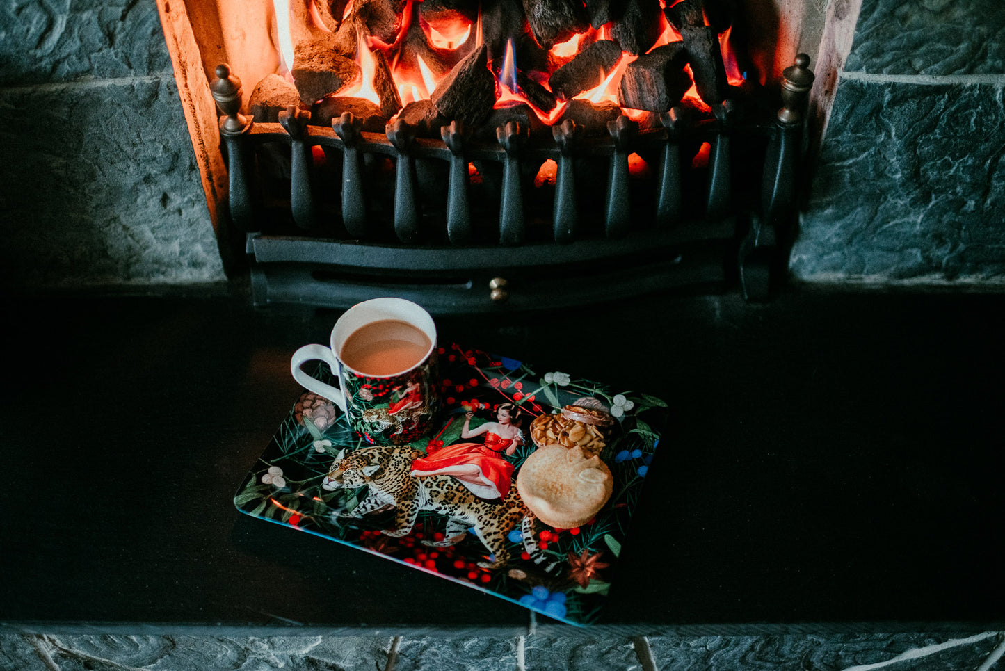 A secondary view of a Luxury bone china coffee cup in a maximalist festive animal fairytale design called - Festive Mary on a tray in front of a fireplace