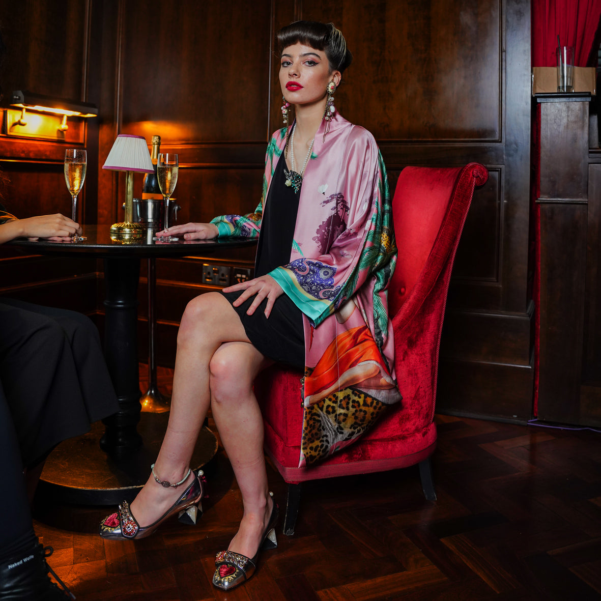 Female model seated in a Bar wearing a luxury 100% silk Kimono in a maximalist vintage pink design