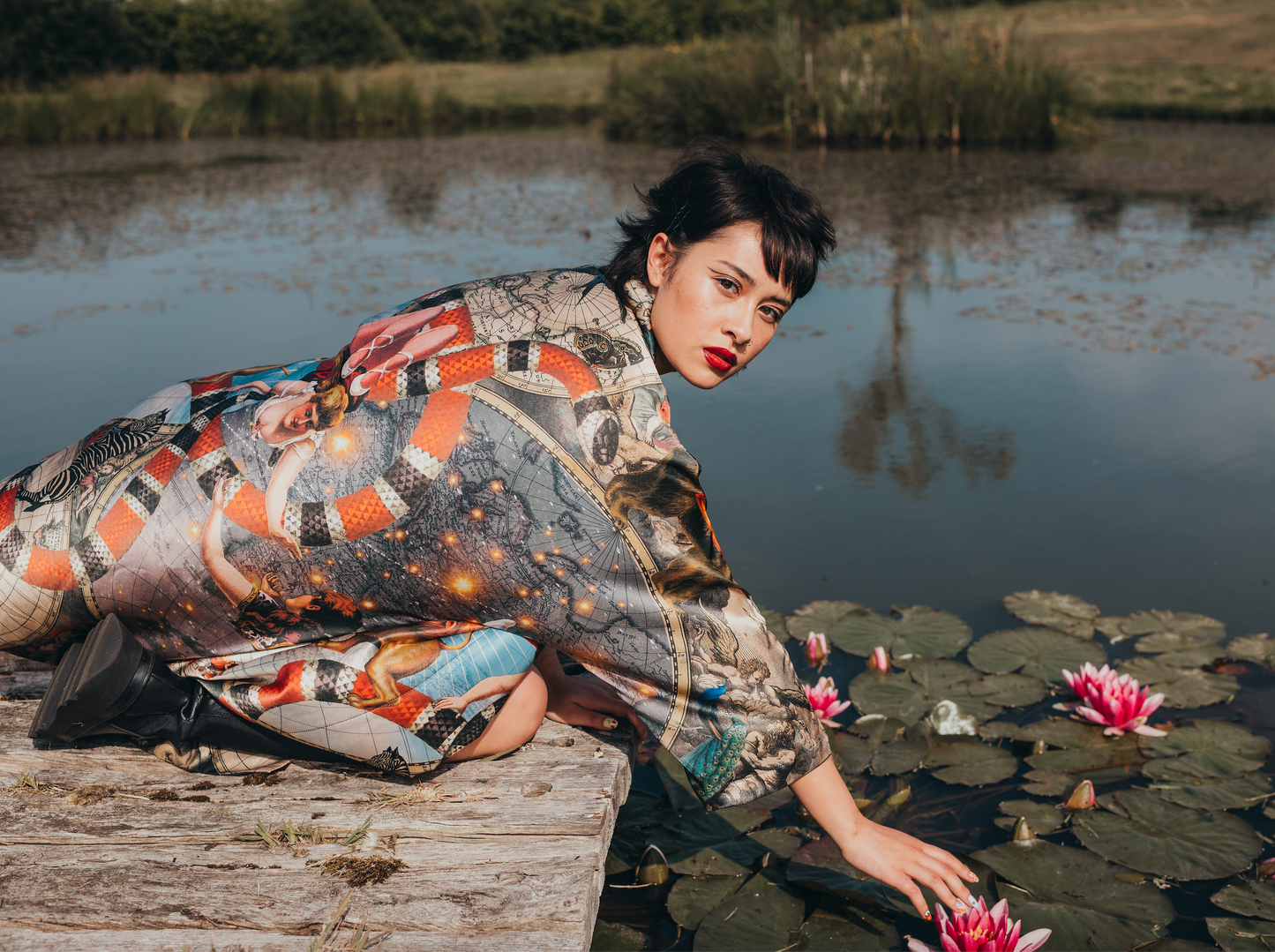 A female model by a pond wearing a luxury 100% silk kimono in a maximalist Vintage Circus design