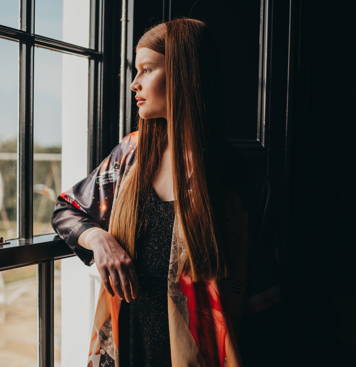 A female model looking out a window wearing a luxury 100% silk kimono in a maximalist retro Pin Up design