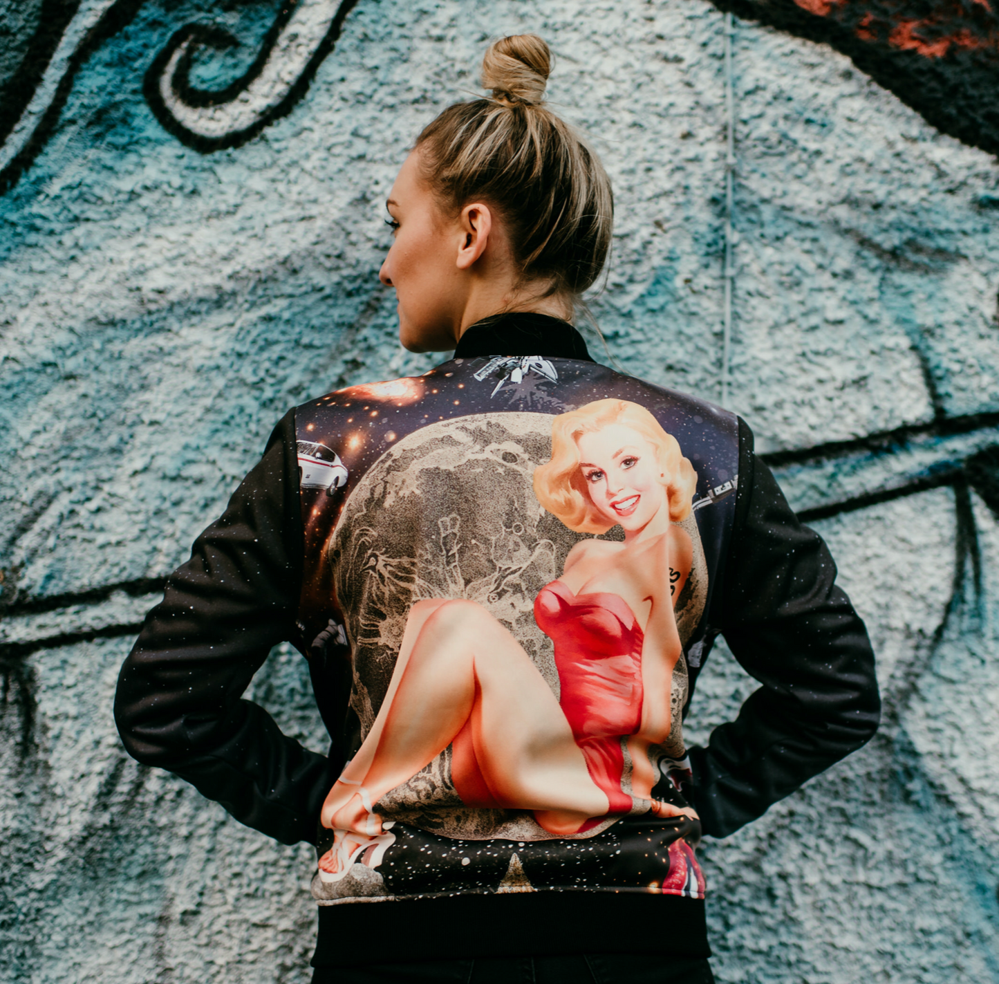 A female model showing back view of luxury softshell bomber jacket in a maximalist retro Pin Up design 