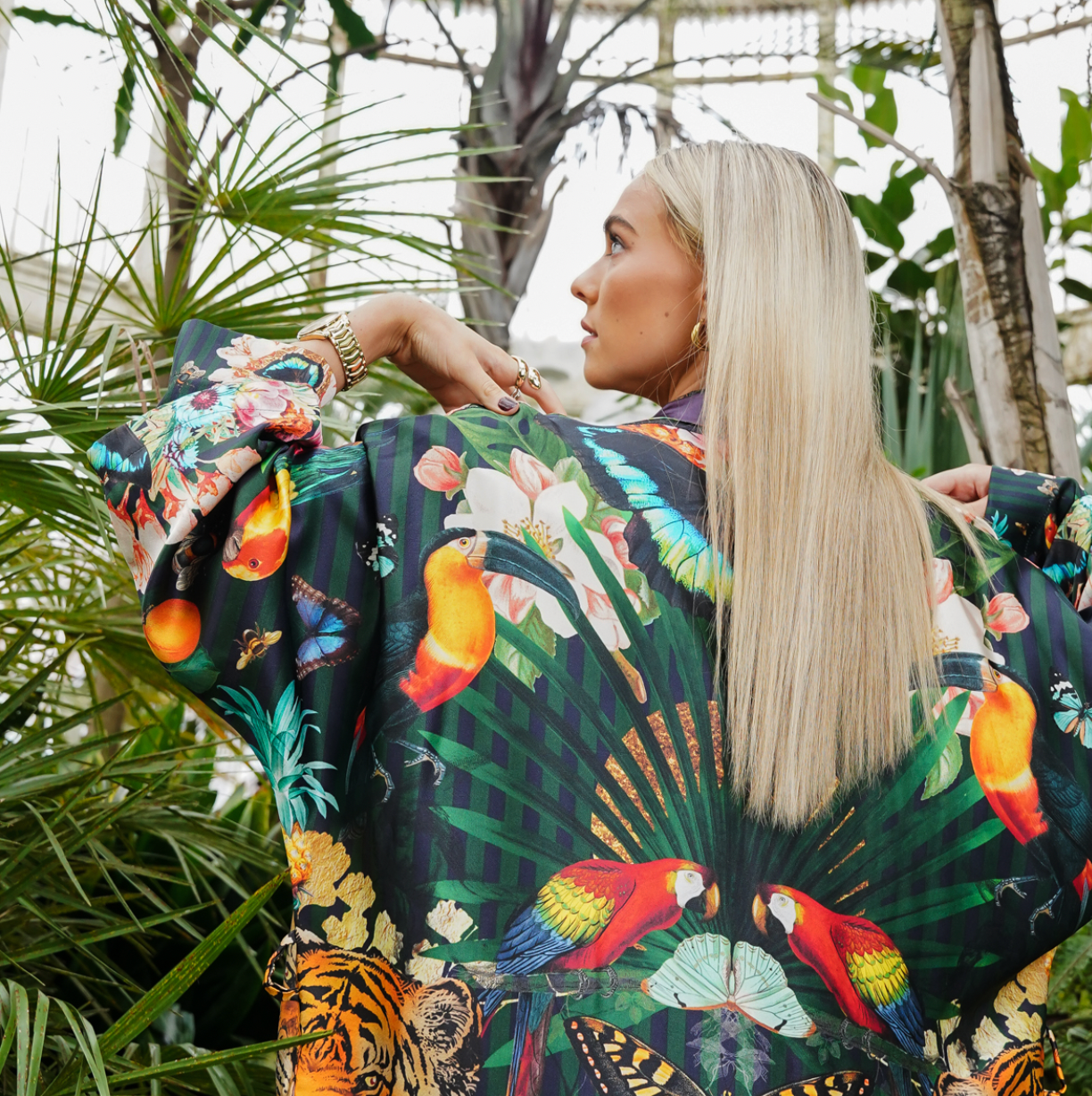 A female model showing the detailed back view of luxury 100% silk Kimono in a maximalist tropical inspired design against a dark background
