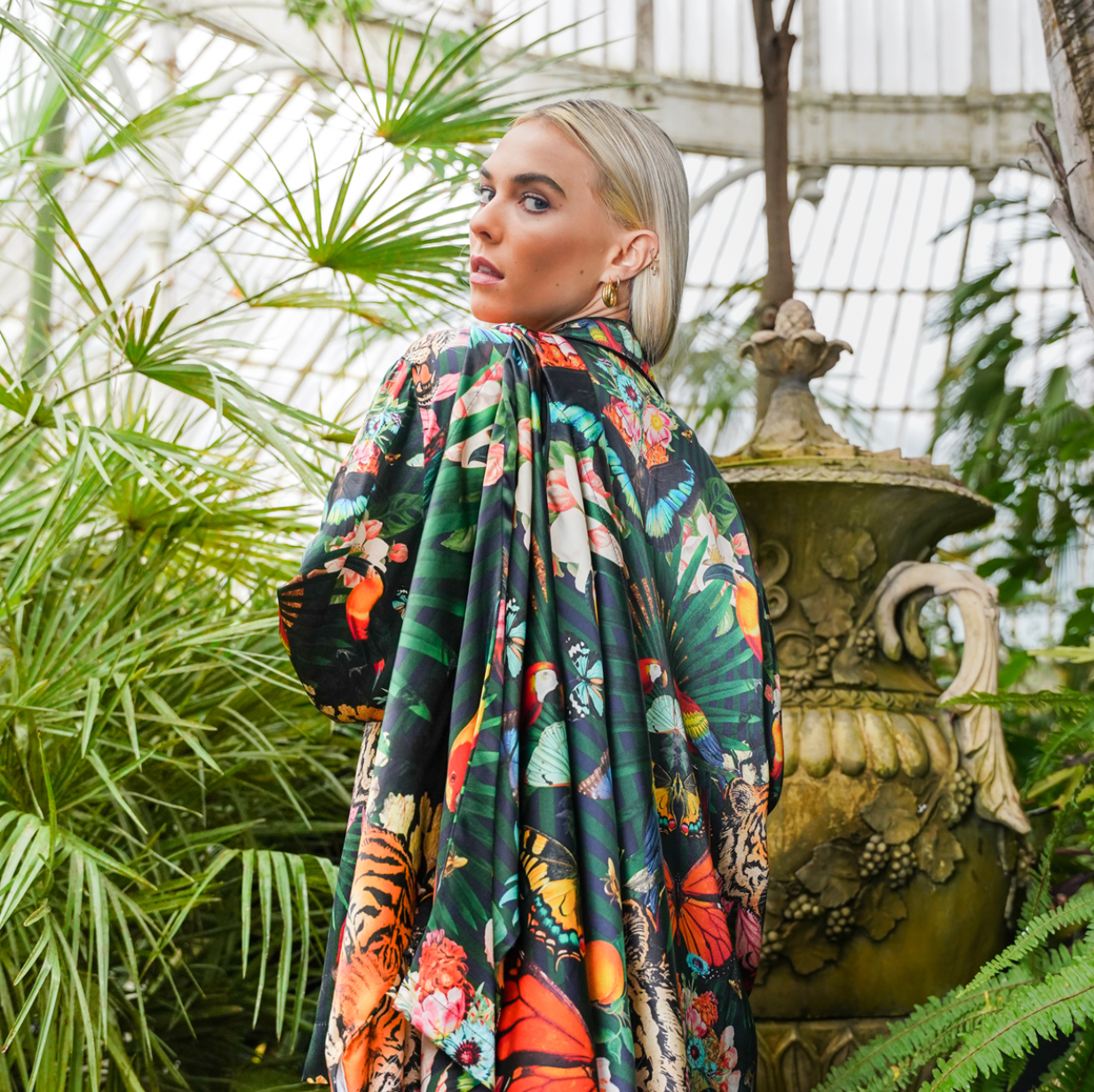 A female model with luxury 100% silk Kimono draped over her shoulder in a maximalist tropical inspired design against a dark background