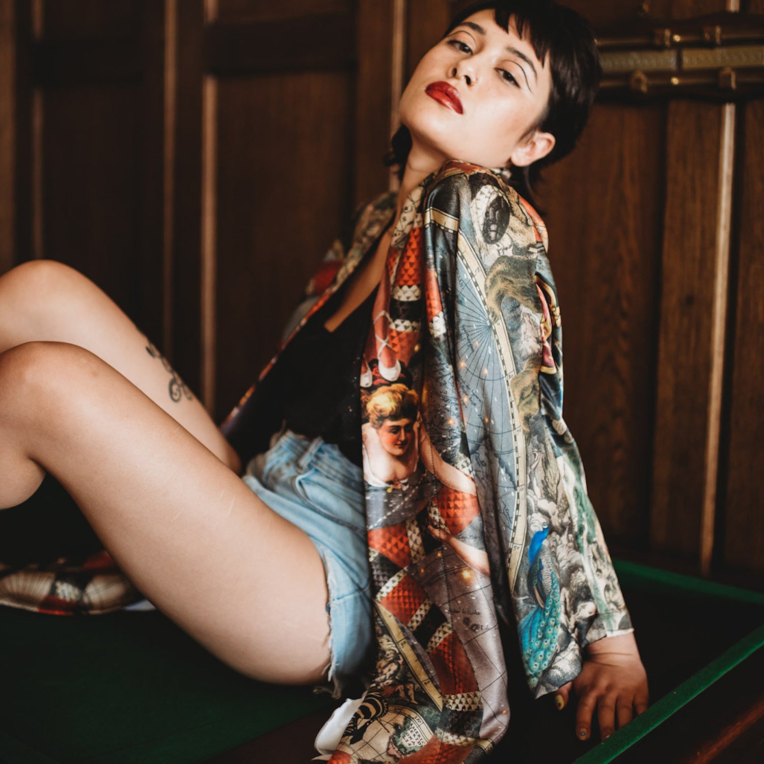 A female model sitting on a pool table wearing a luxury 100% silk kimono in a maximalist Vintage Circus design