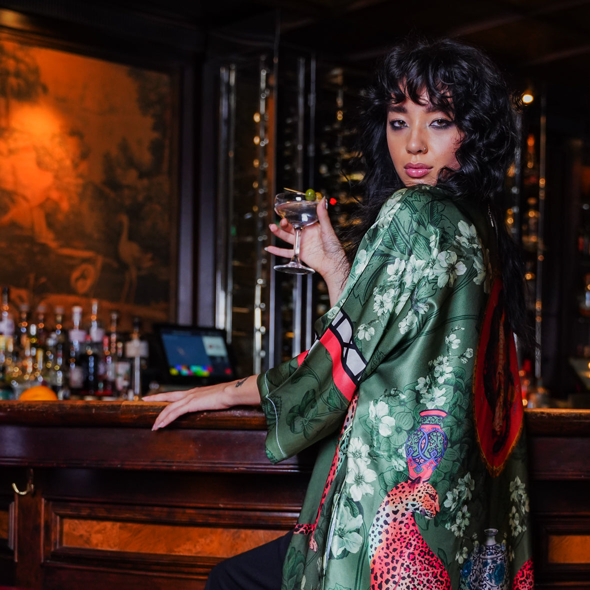 Female model at a Bar wearing luxury 100% silk Kimono in a green maximalist oriental inspired design 